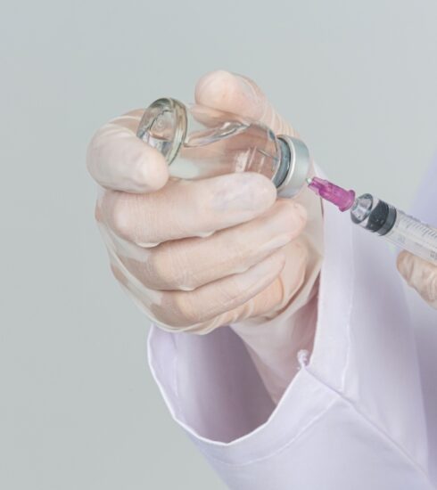 Young doctor is holding hypodermic syringe with vaccine vial rubber gloves gray wall 1 850x560